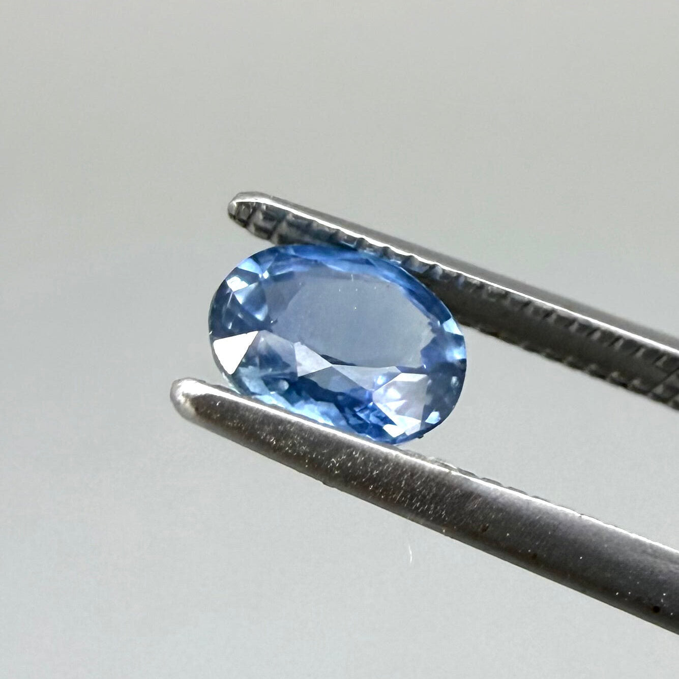 0.84 ct natural bright-blue sapphire from Bangkaja, oval cut, shown held with tweezers.