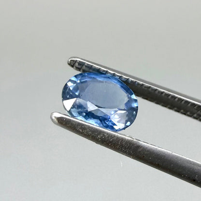 0.84 ct natural bright-blue sapphire from Bangkaja, oval cut, shown held with tweezers.