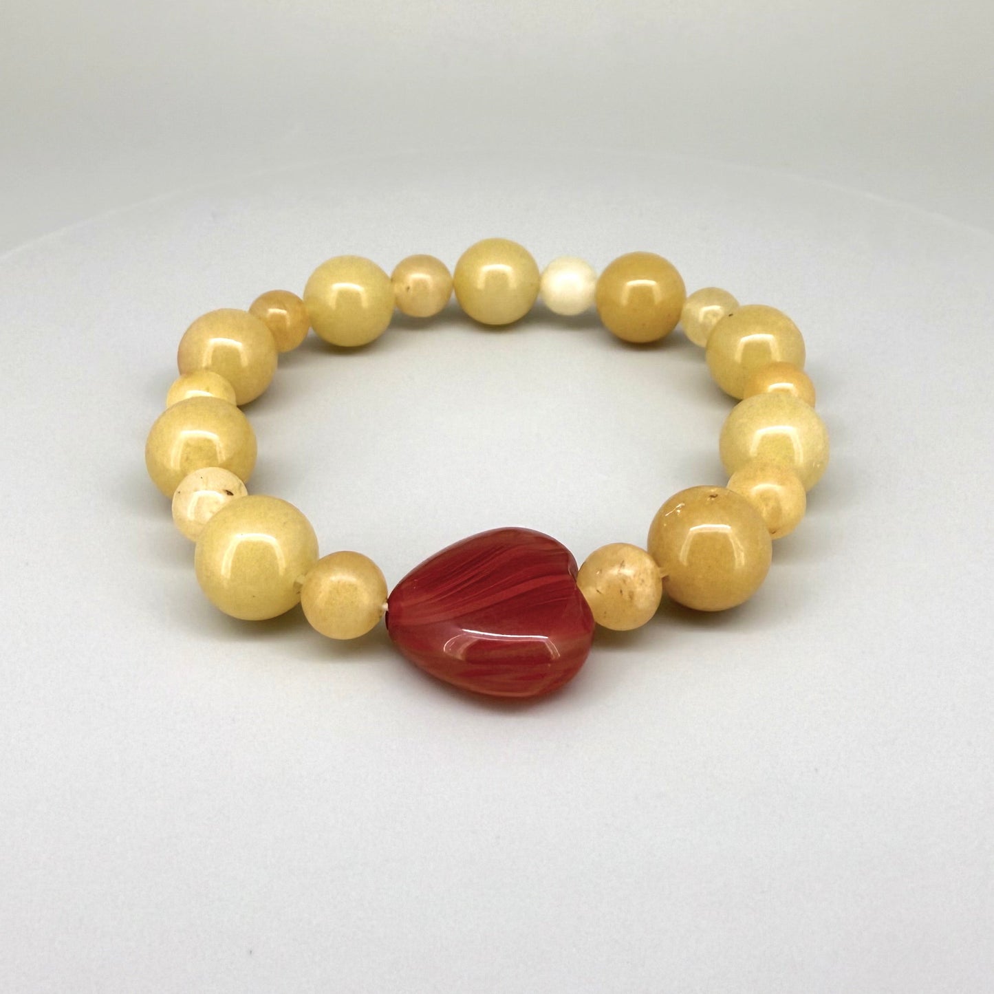 Jade and carnelian beaded bracelet, 20cm, yellow-cream jade beads with large heart-shaped orange-red carnelian focal stone on elastic stretch band.