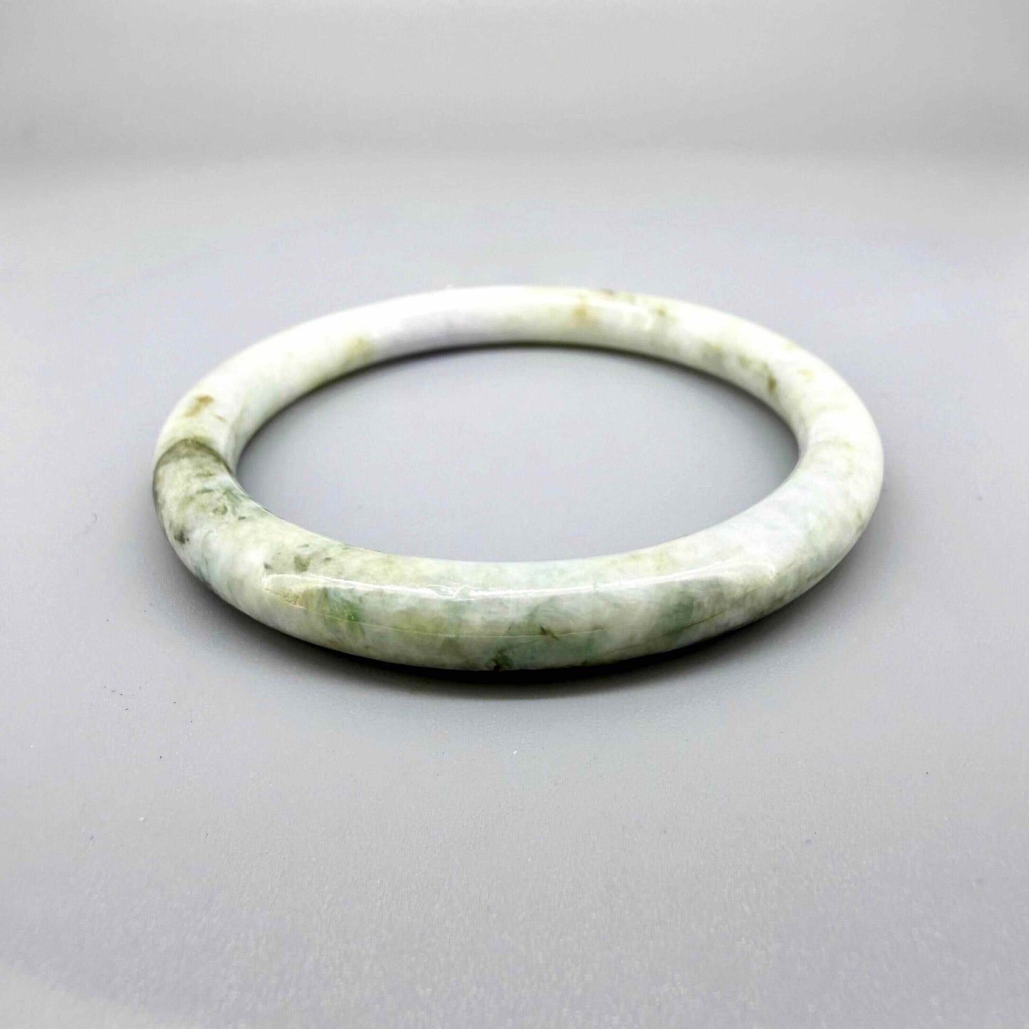 Polished jade bangle in soft green hues with smooth surface and natural variations