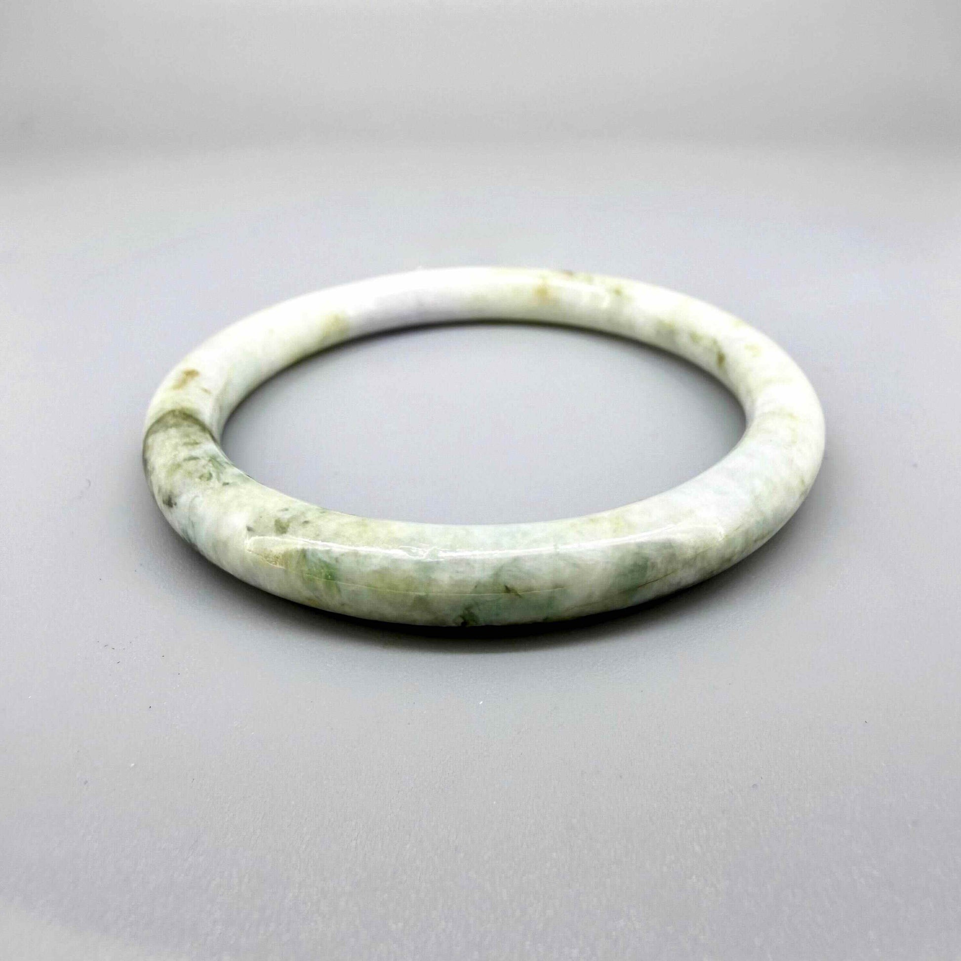 Polished jade bangle in soft green hues with smooth surface and natural variations