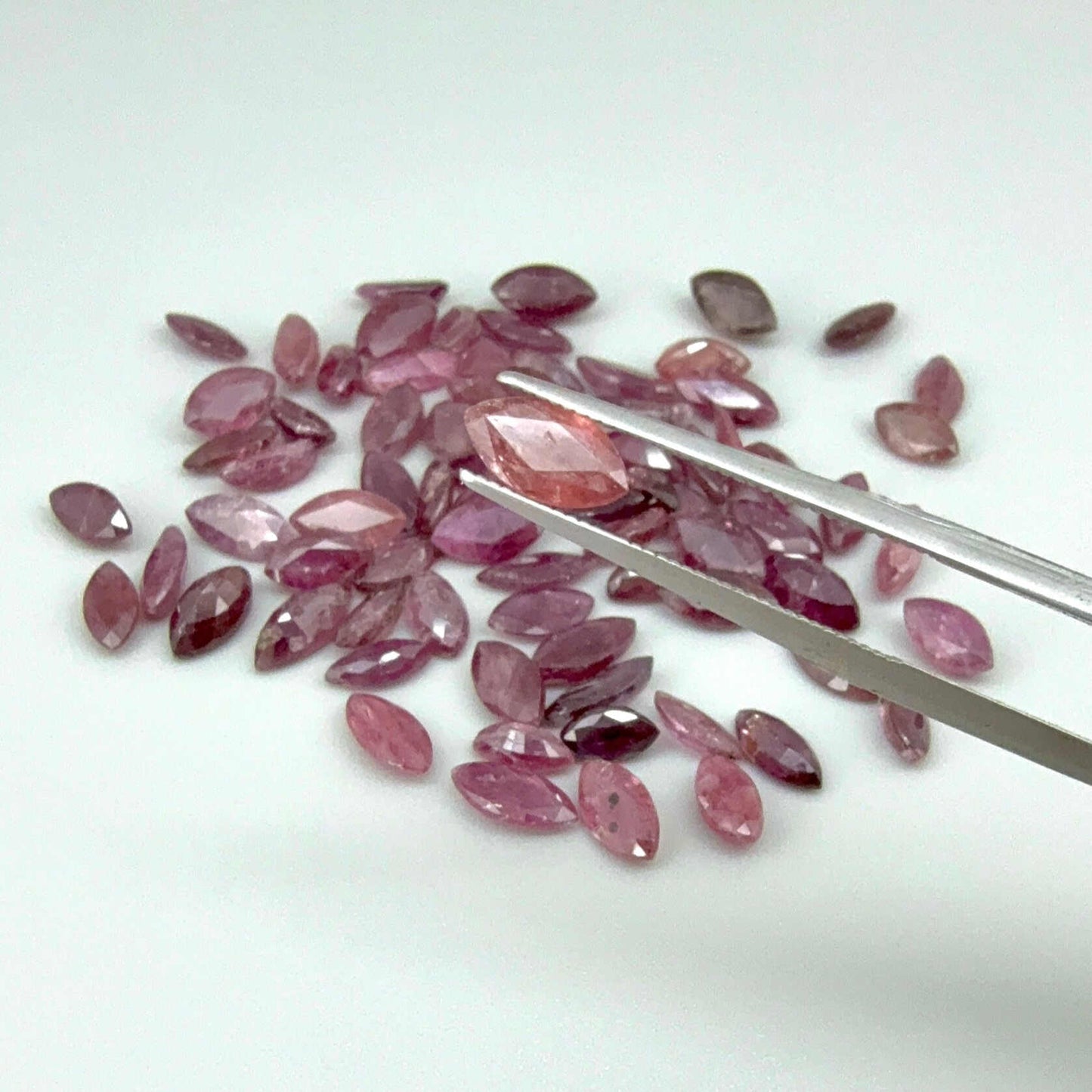 Pink gemstones with a pair of tweezers on a white background

