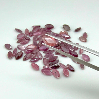 Pink gemstones with a pair of tweezers on a white background

