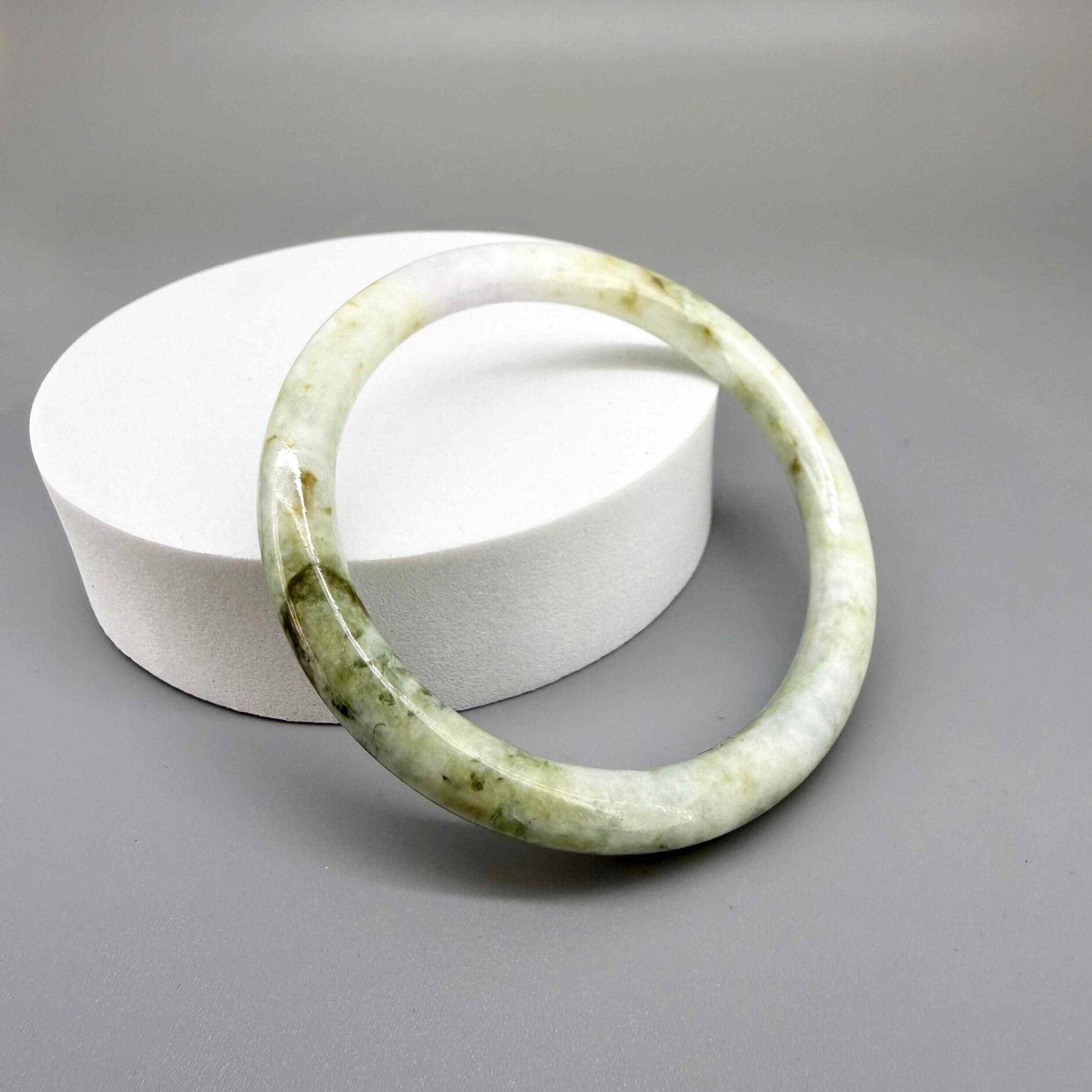 Polished jade bangle in soft green hues with smooth surface and natural variations