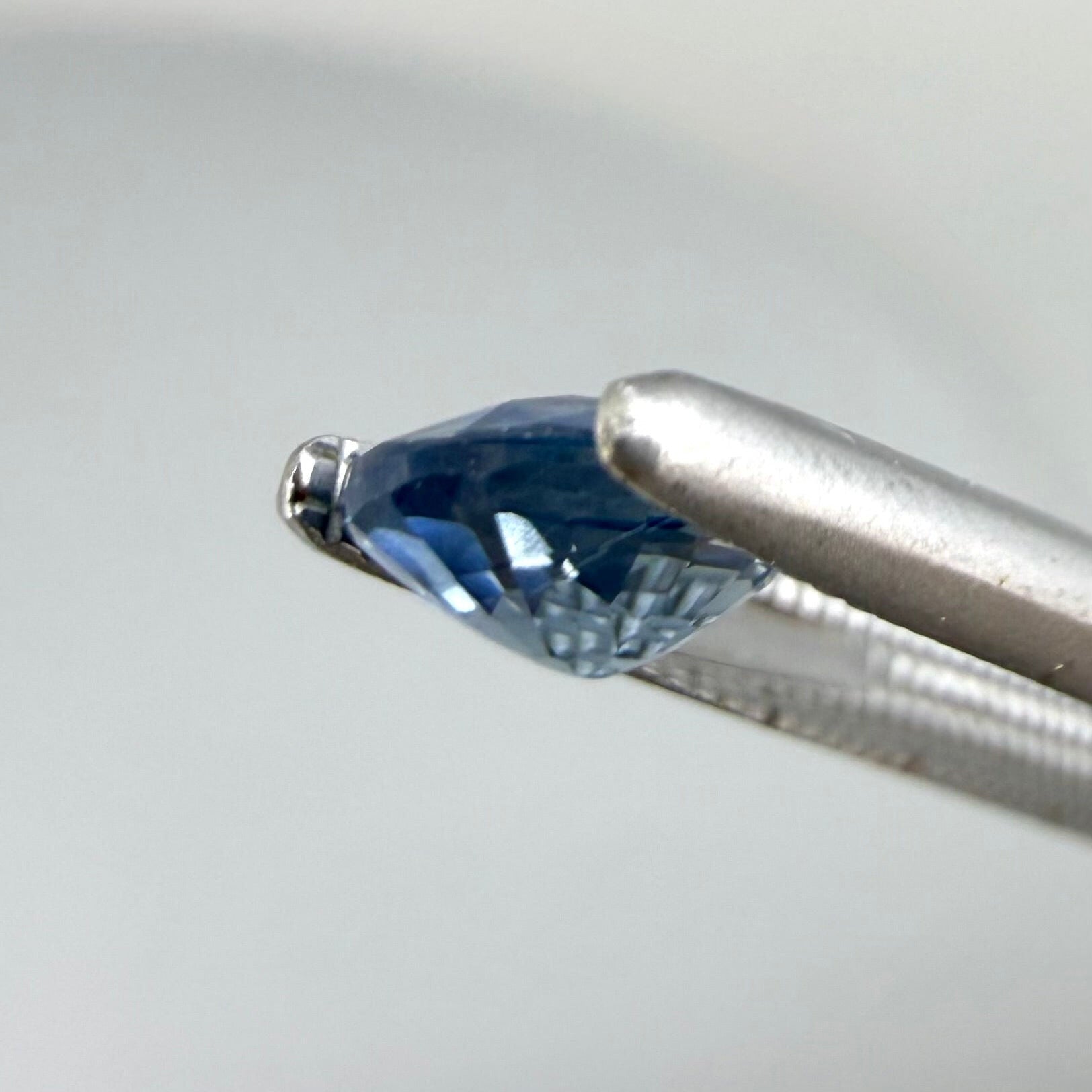 0.84 ct natural bright-blue sapphire from Bangkaja, oval cut, shown held with tweezers.