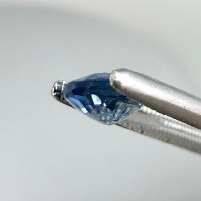 0.84 ct natural bright-blue sapphire from Bangkaja, oval cut, shown held with tweezers.