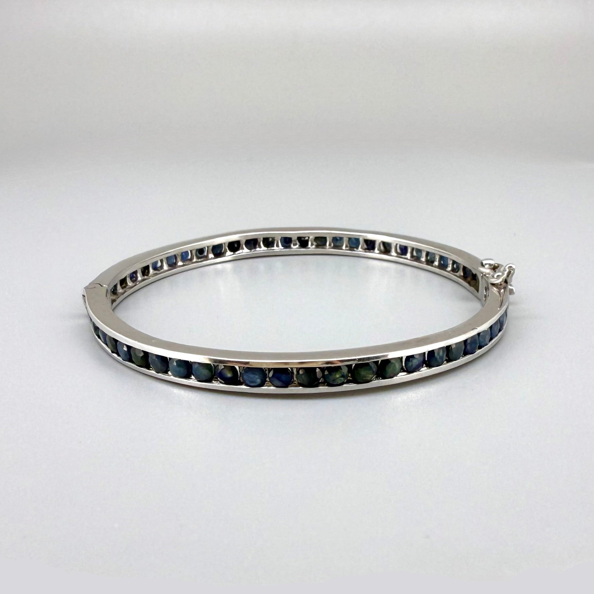 Blue sapphire bangle in sterling silver with white gold plating on neutral background