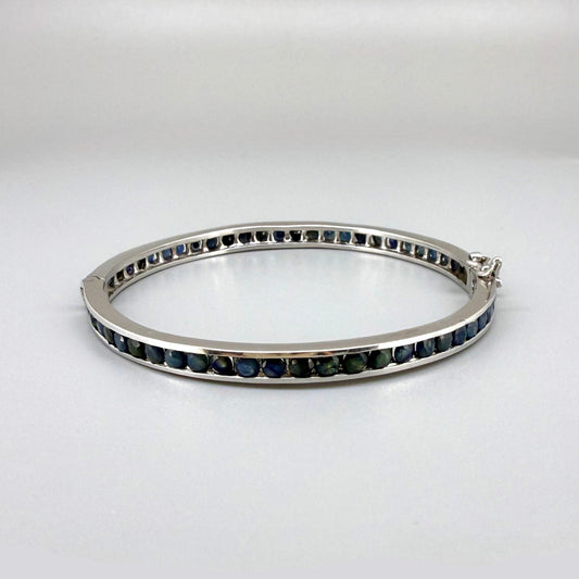 Blue sapphire bangle in sterling silver with white gold plating on neutral background
