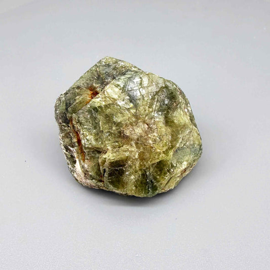 Natural rough green sapphire, opaque, uncut and irregular, showing olive to moss-green tones, photographed in hand on neutral background.
