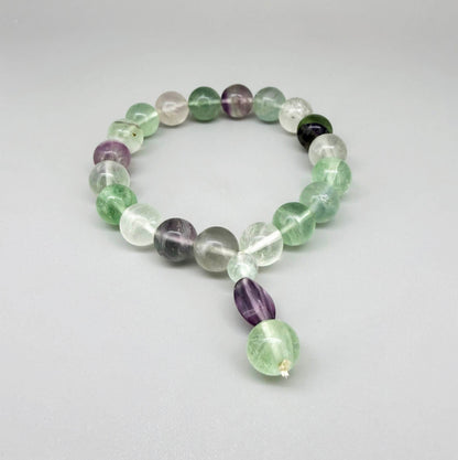 Fluorite mala bracelet with green and purple translucent gemstone beads and decorative charm detail.