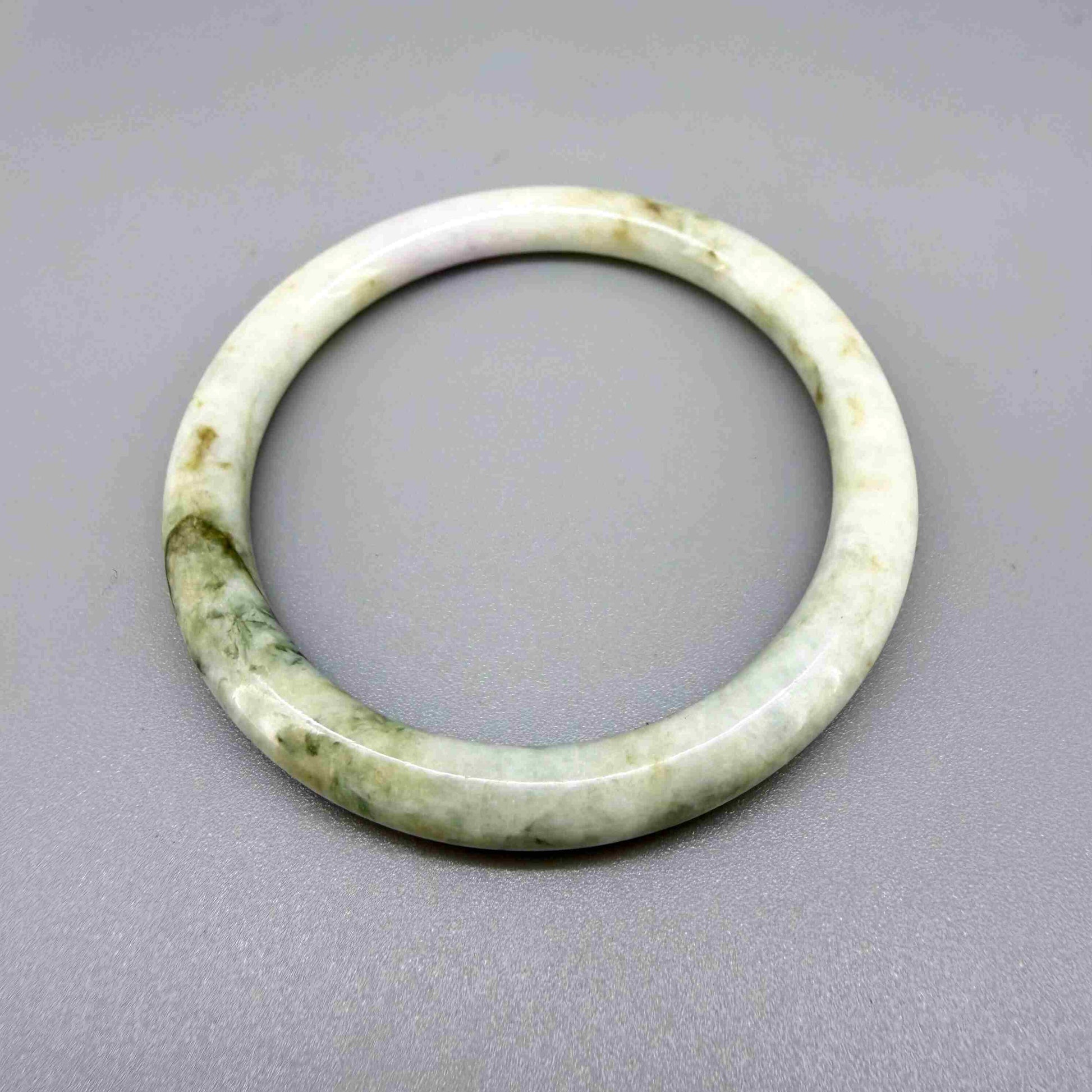 Polished jade bangle in soft green hues with smooth surface and natural variations