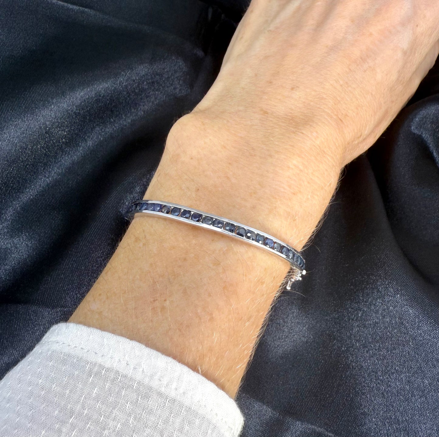 Blue sapphire bangle in sterling silver with white gold plating on neutral background worn on wrist