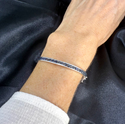 Blue sapphire bangle in sterling silver with white gold plating on neutral background worn on wrist