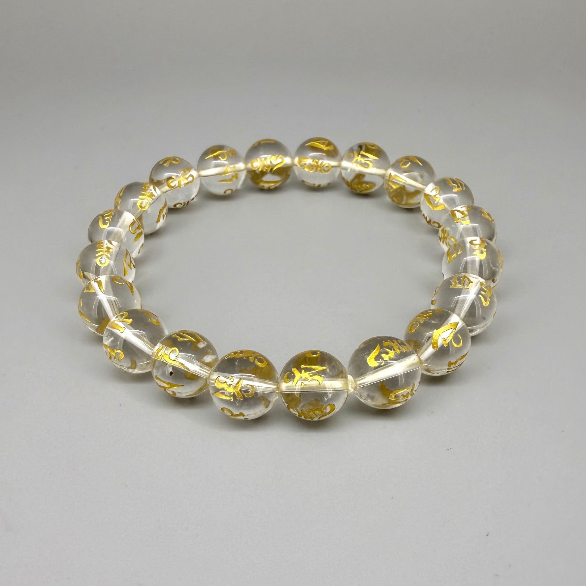 Clear quartz beaded bracelet, 19cm, transparent gemstone beads engraved with golden Sanskrit mantra Om Mani Padme Hum on elastic stretch band.