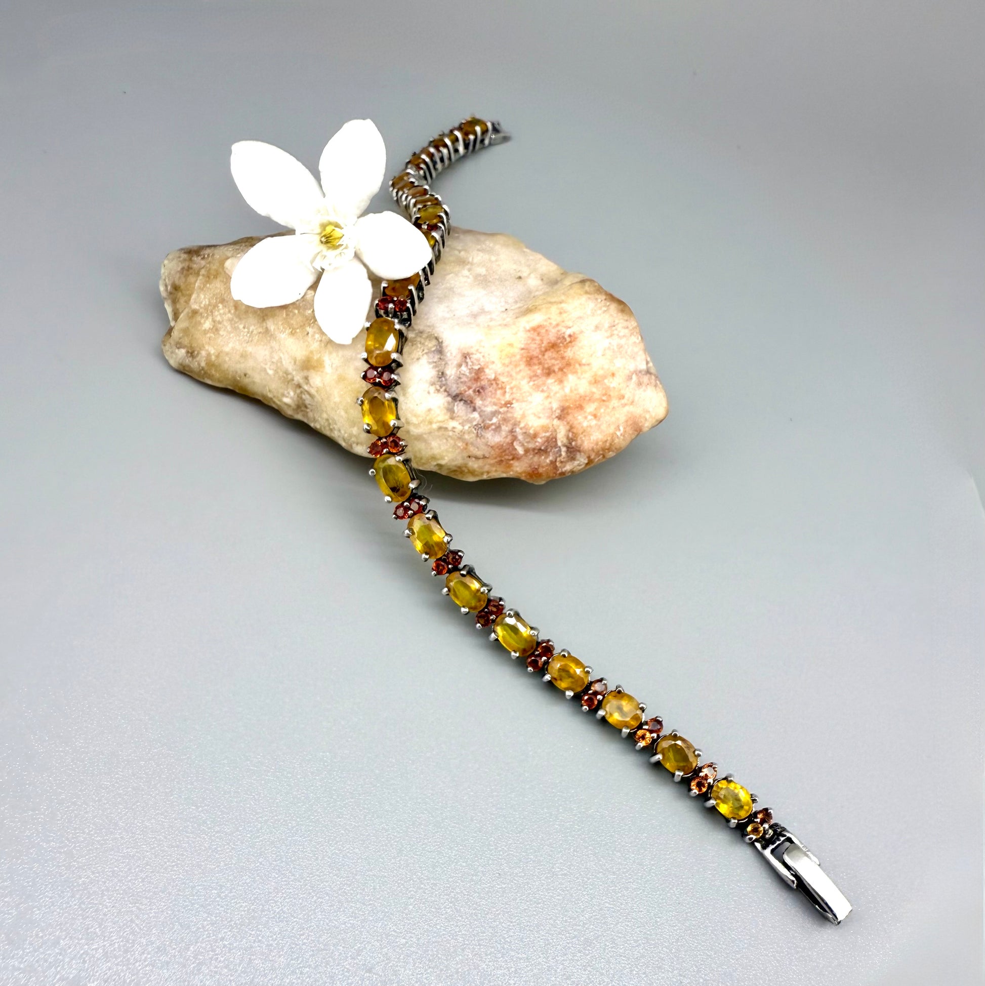 White gold plated sapphire bracelet in yellow, orange, and red hues on neutral background