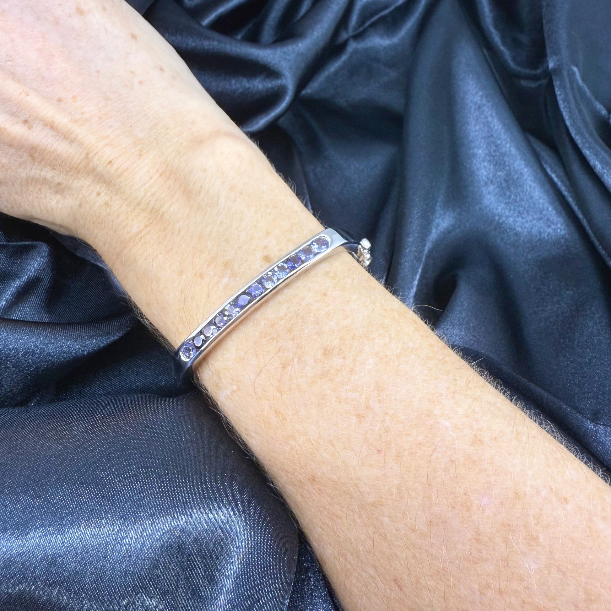 White gold plated sterling silver bangle with faceted natural iolite gemstones in violet-blue tones.