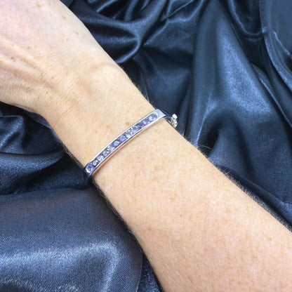 White gold plated sterling silver bangle with faceted natural iolite gemstones in violet-blue tones.