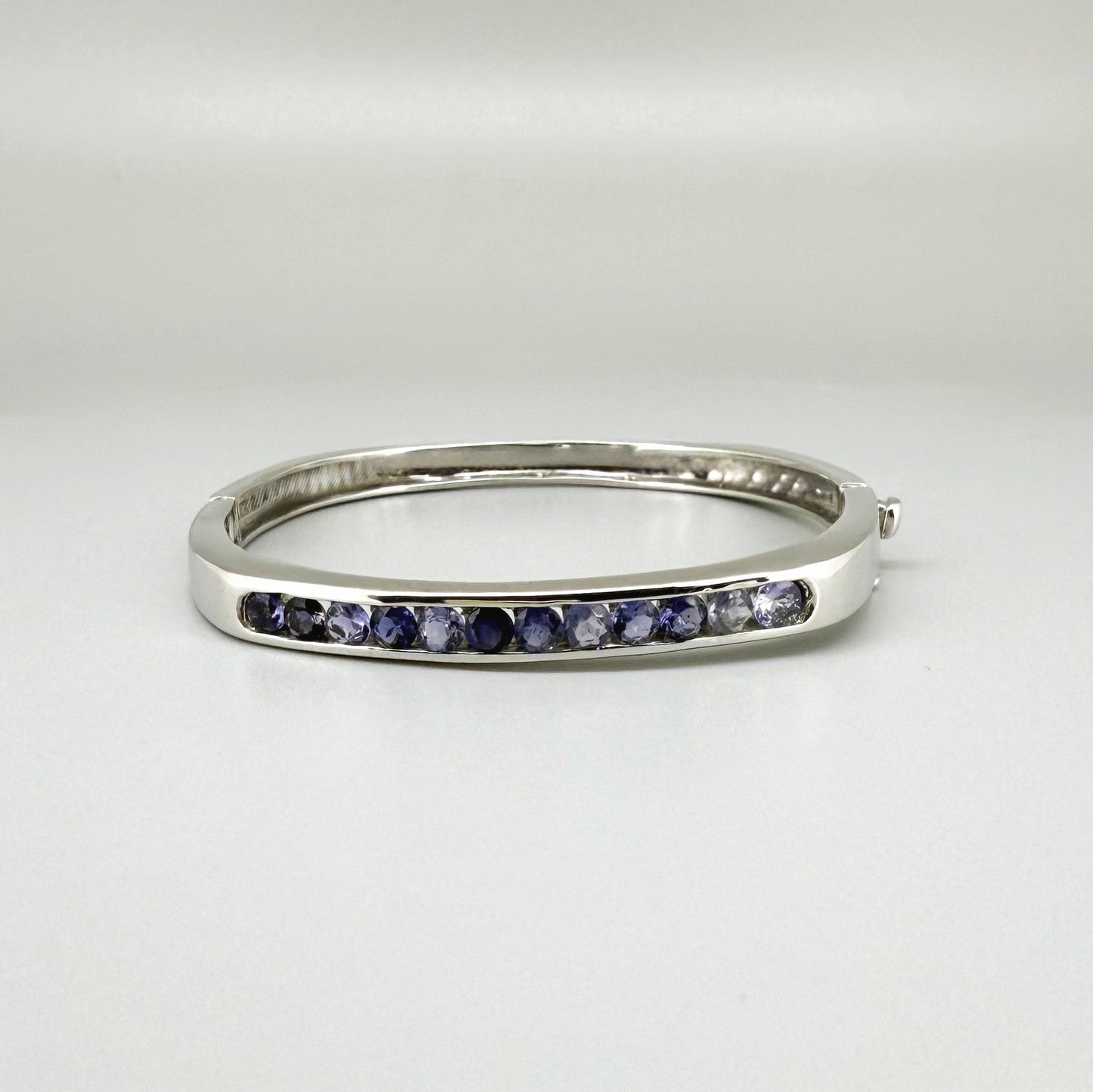 White gold plated sterling silver bangle with faceted natural iolite gemstones in violet-blue tones.