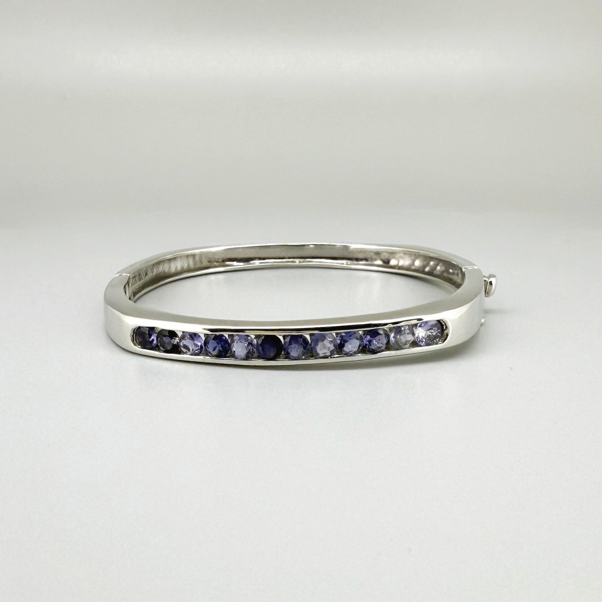 White gold plated sterling silver bangle with faceted natural iolite gemstones in violet-blue tones.