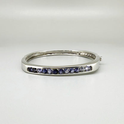White gold plated sterling silver bangle with faceted natural iolite gemstones in violet-blue tones.