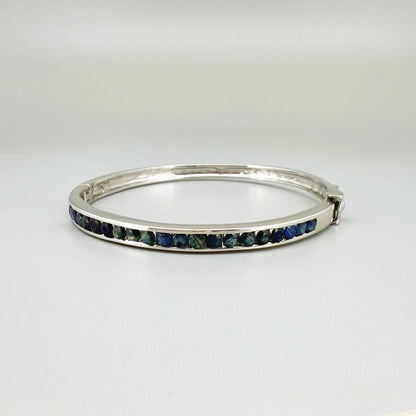 Blue sapphire bangle in white gold plated sterling silver with faceted deep blue gemstones.