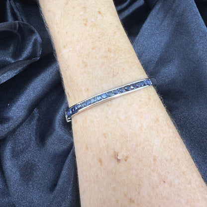 Blue sapphire bangle in white gold plated sterling silver with faceted deep blue gemstones.