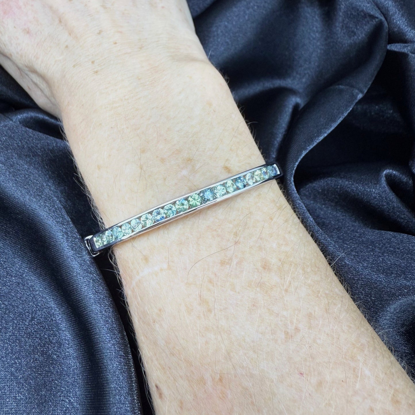 White gold plated silver bangle set with faceted natural green sapphires.