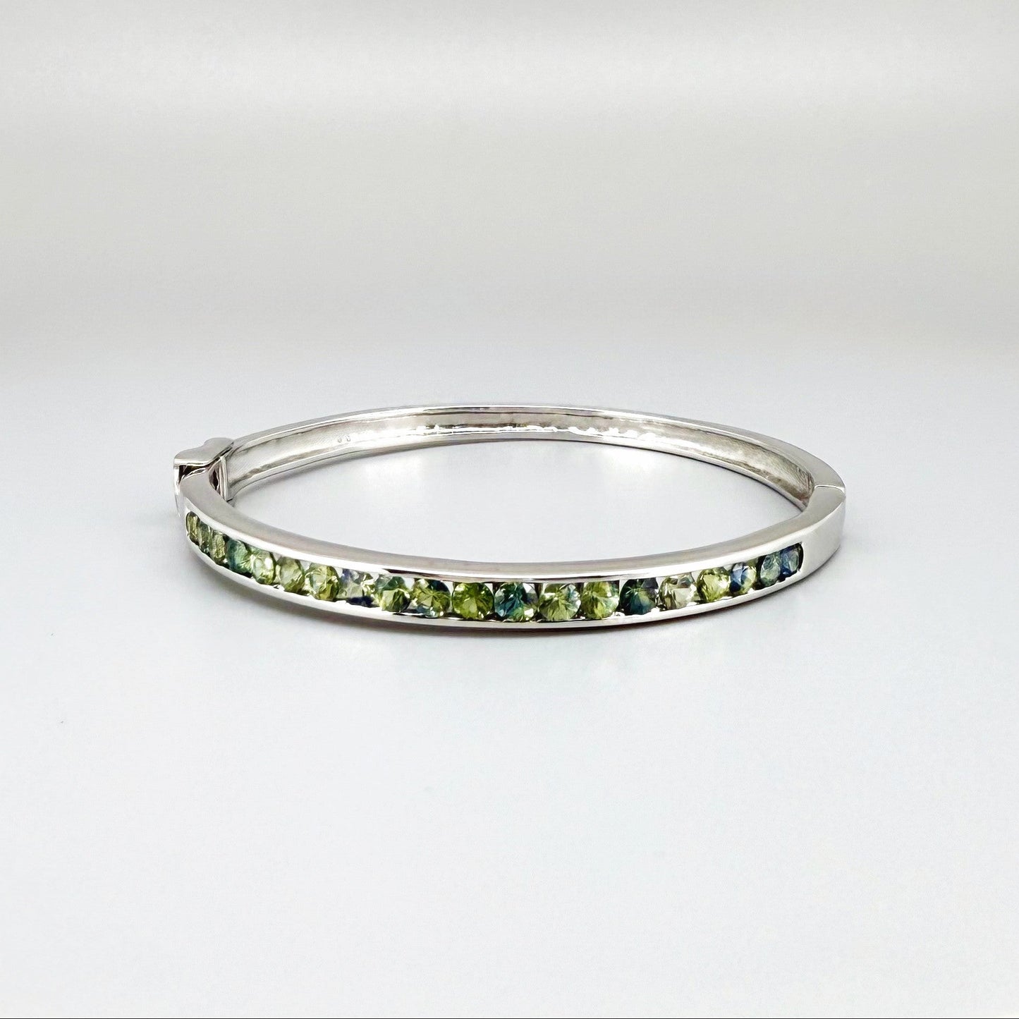 White gold plated silver bangle set with faceted natural green sapphires.