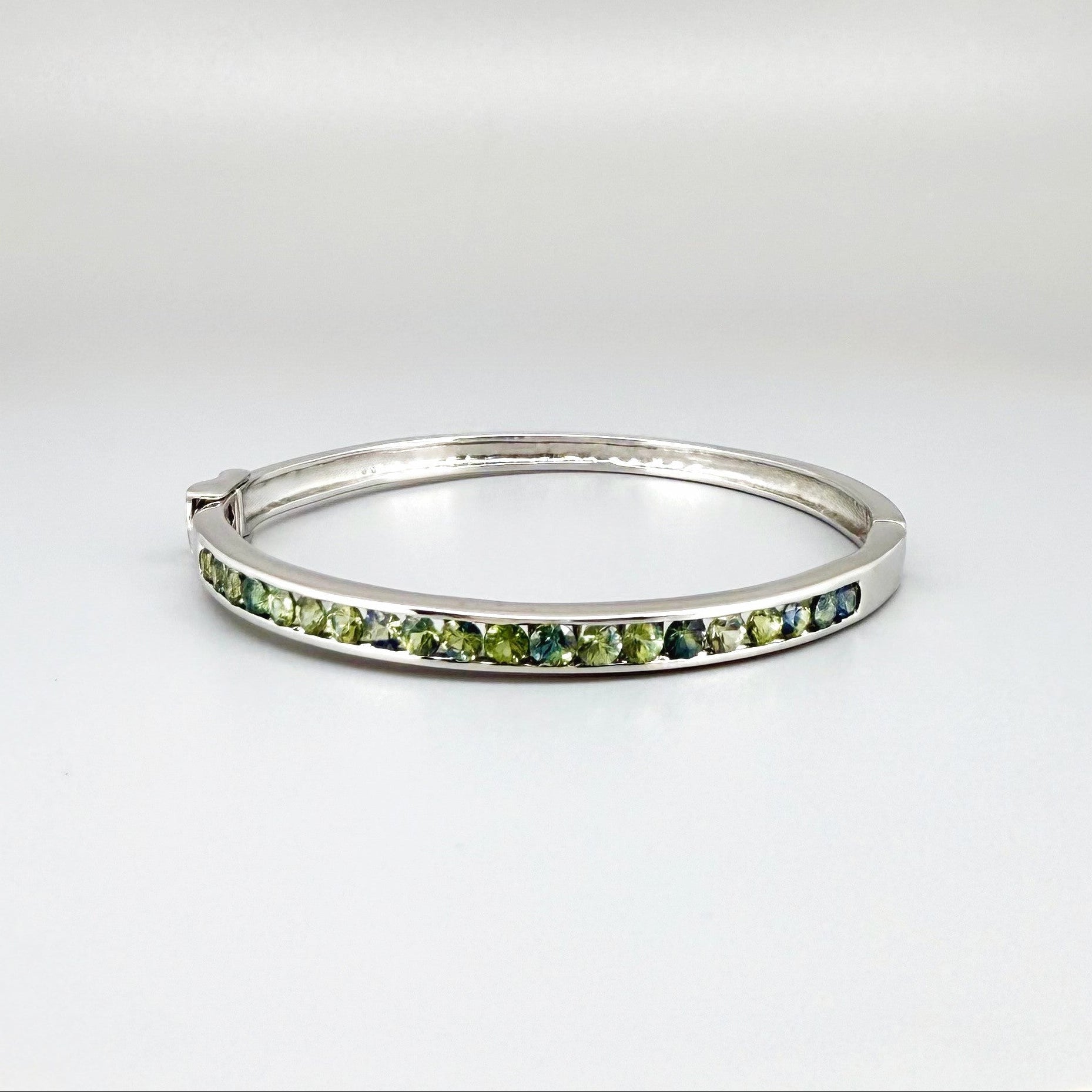 White gold plated silver bangle set with faceted natural green sapphires.