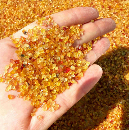 Natural sapphire rough with warm yellow-orange hues and subtle color variation, uncut corundum photographed on neutral background.