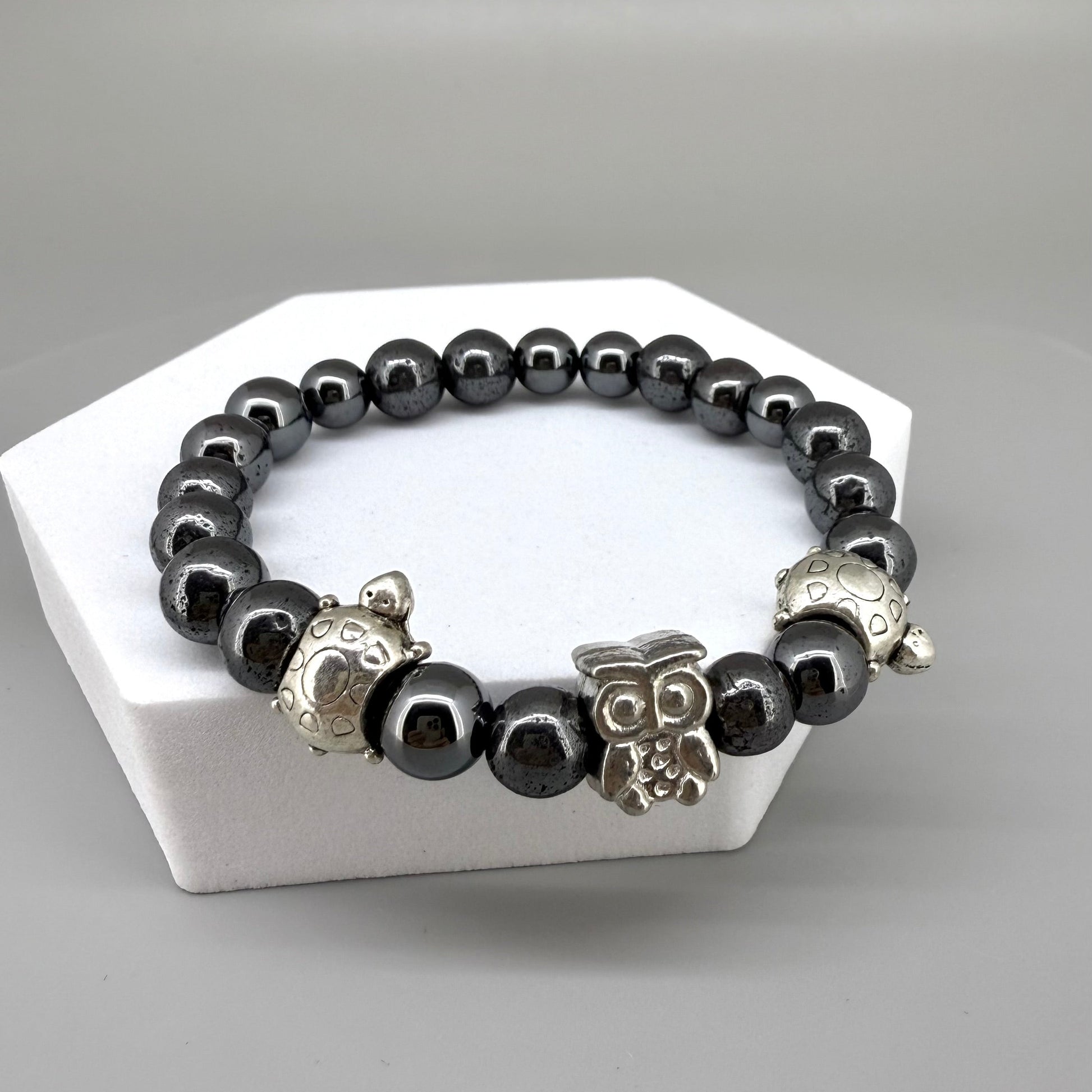 Hematite beaded bracelet, 18cm, metallic dark grey gemstone beads with two turtle accents and one owl charm on elastic stretch band.