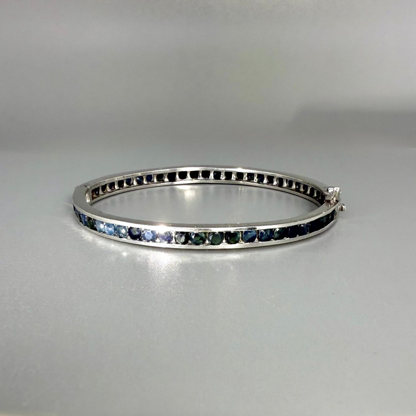 Blue sapphire bangle in sterling silver with white gold plating on neutral background