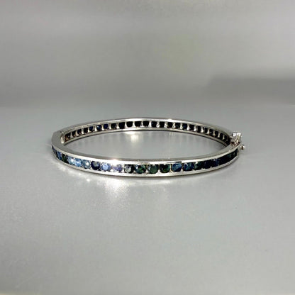 Blue sapphire bangle in sterling silver with white gold plating on neutral background