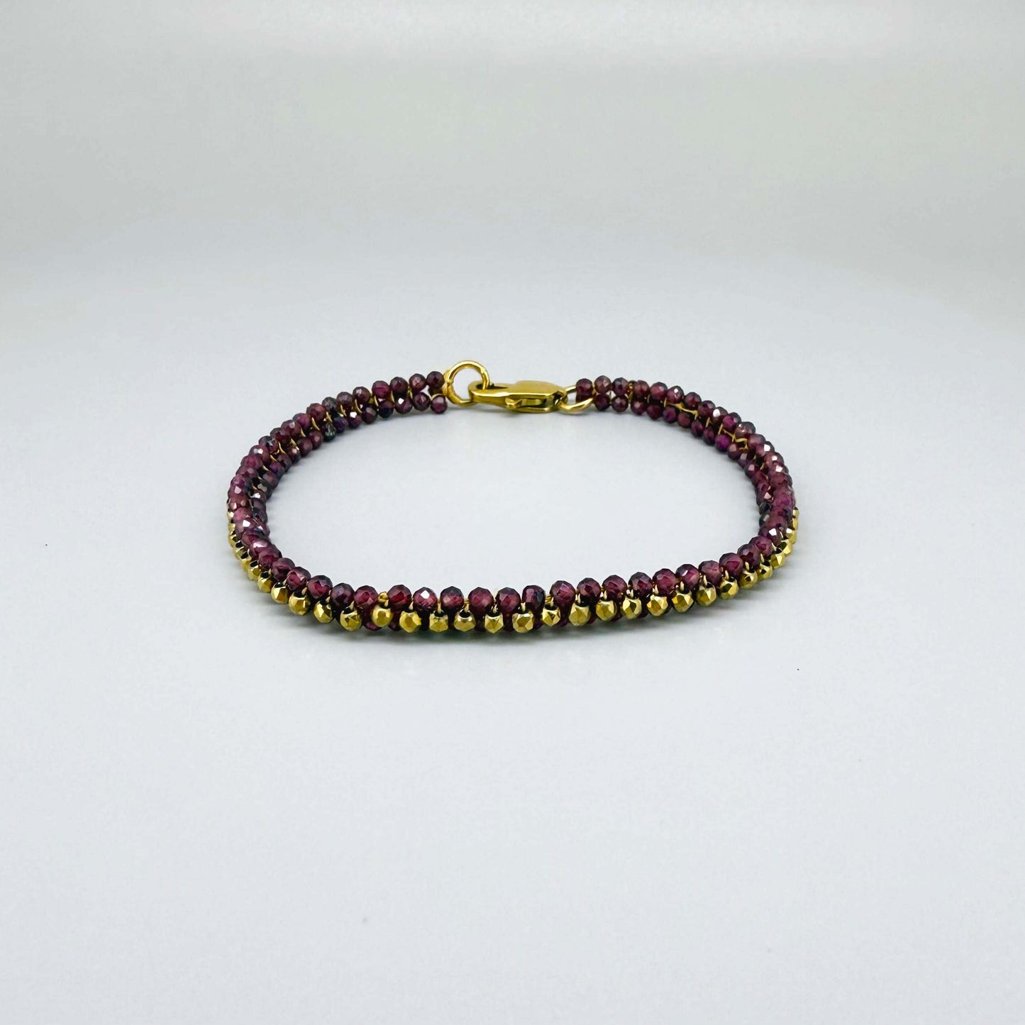 18 cm beaded bracelet made of wine-red garnet and gold-toned hematite with a lobster clasp, displayed on a light background.