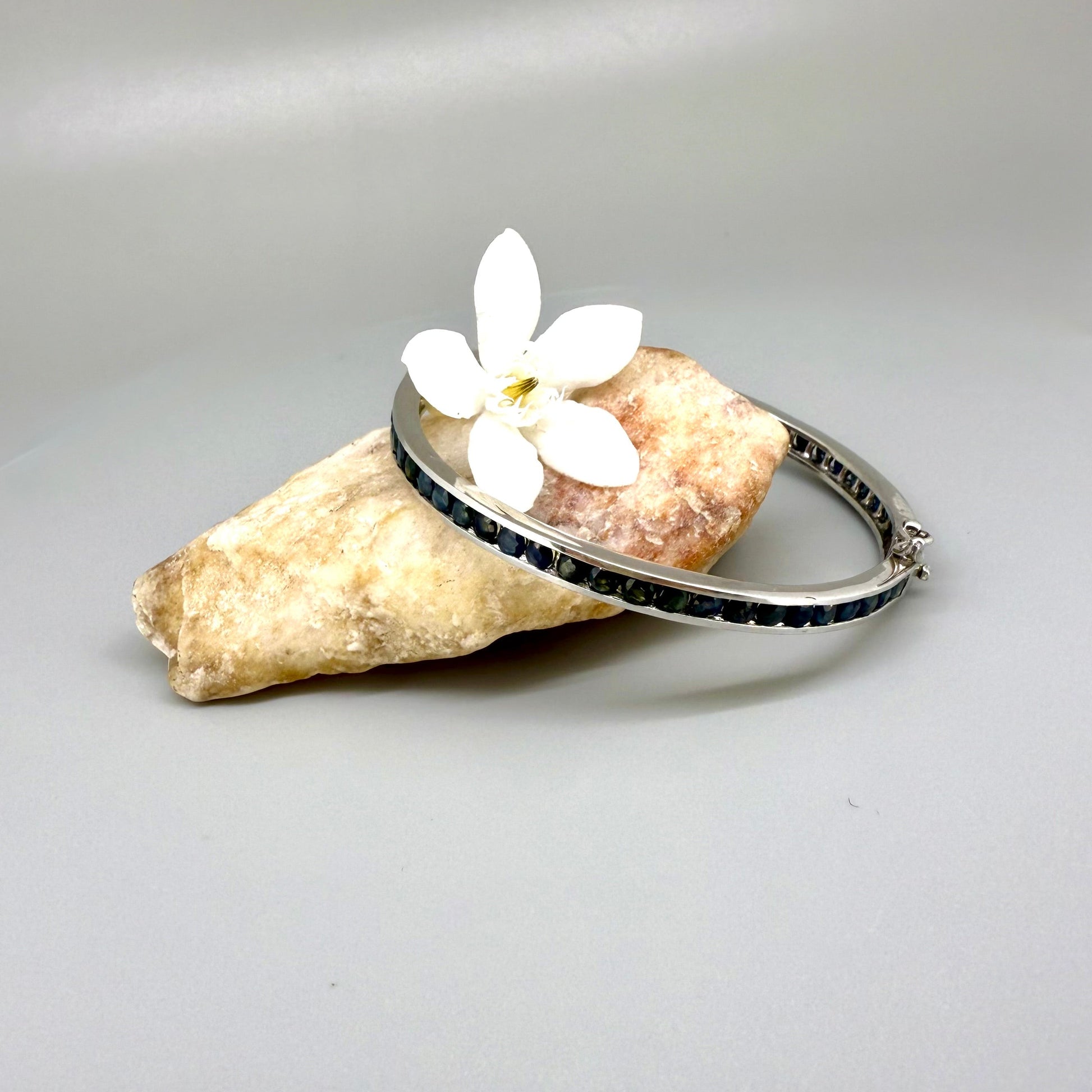 Blue sapphire bangle in sterling silver with white gold plating on neutral background