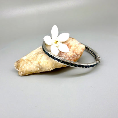 Blue sapphire bangle in sterling silver with white gold plating on neutral background