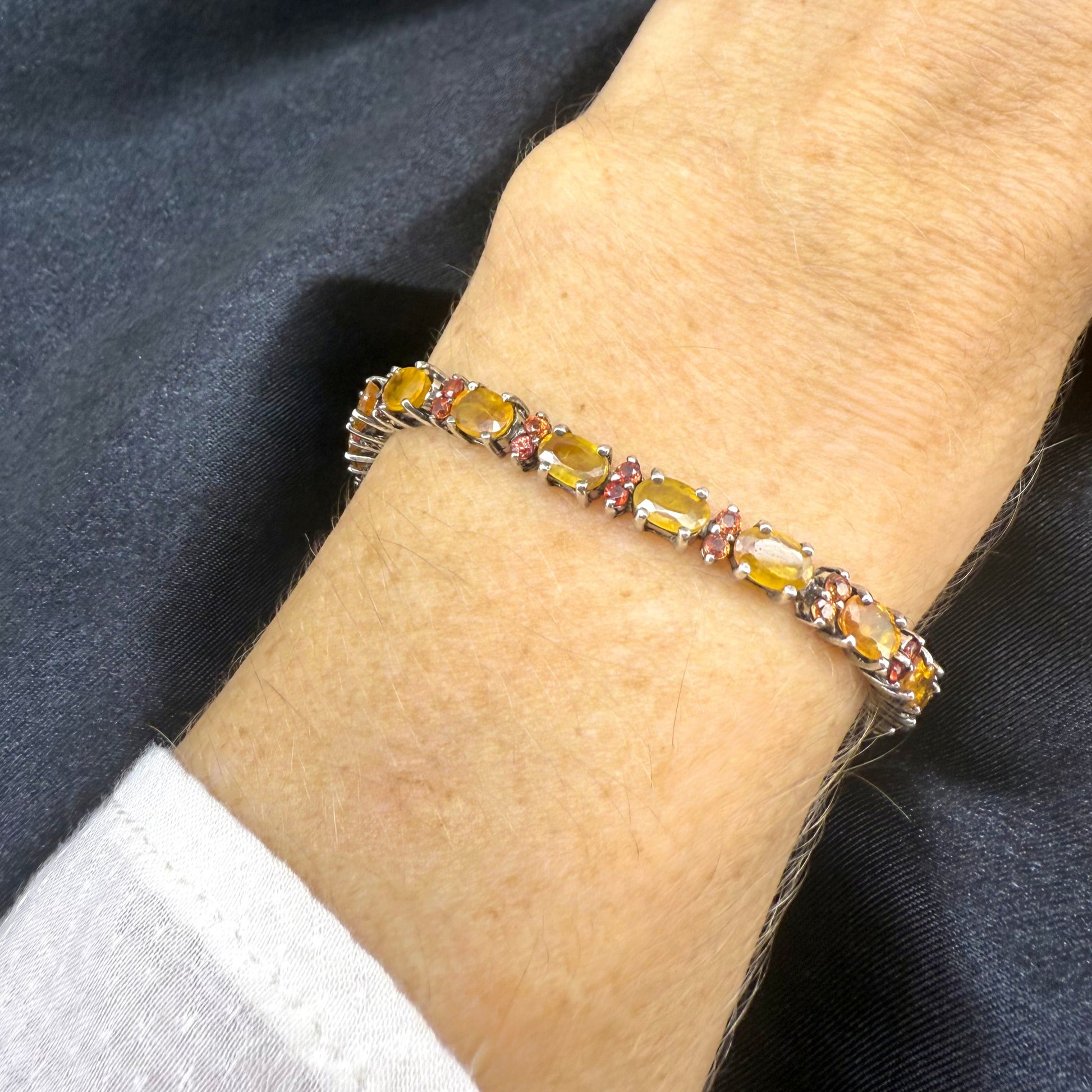 White gold plated sapphire bracelet in yellow, orange, and red hues on neutral background