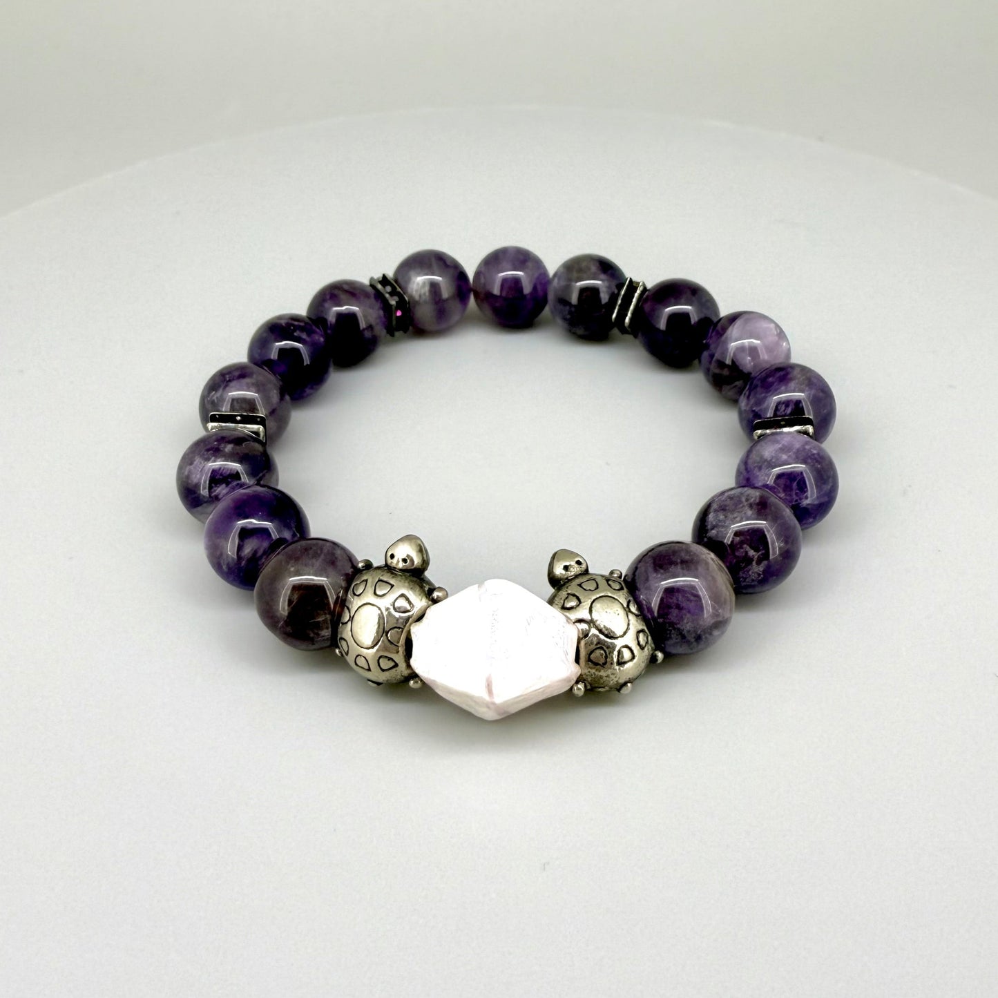 Amethyst beaded bracelet, 18cm, violet gemstone beads with pink-white accent stone and two metal turtle beads on elastic stretch band.