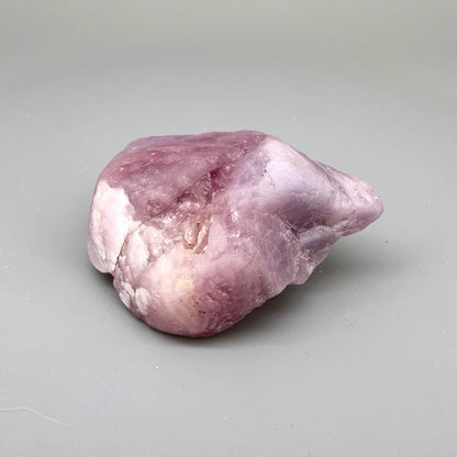 Natural ruby rough stone in soft pink to pale rose tones, uncut corundum specimen photographed on neutral background.