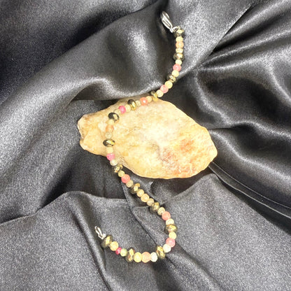 Faceted beaded bracelet with ruby, sapphire, emerald, and pyrite gemstones on neutral background