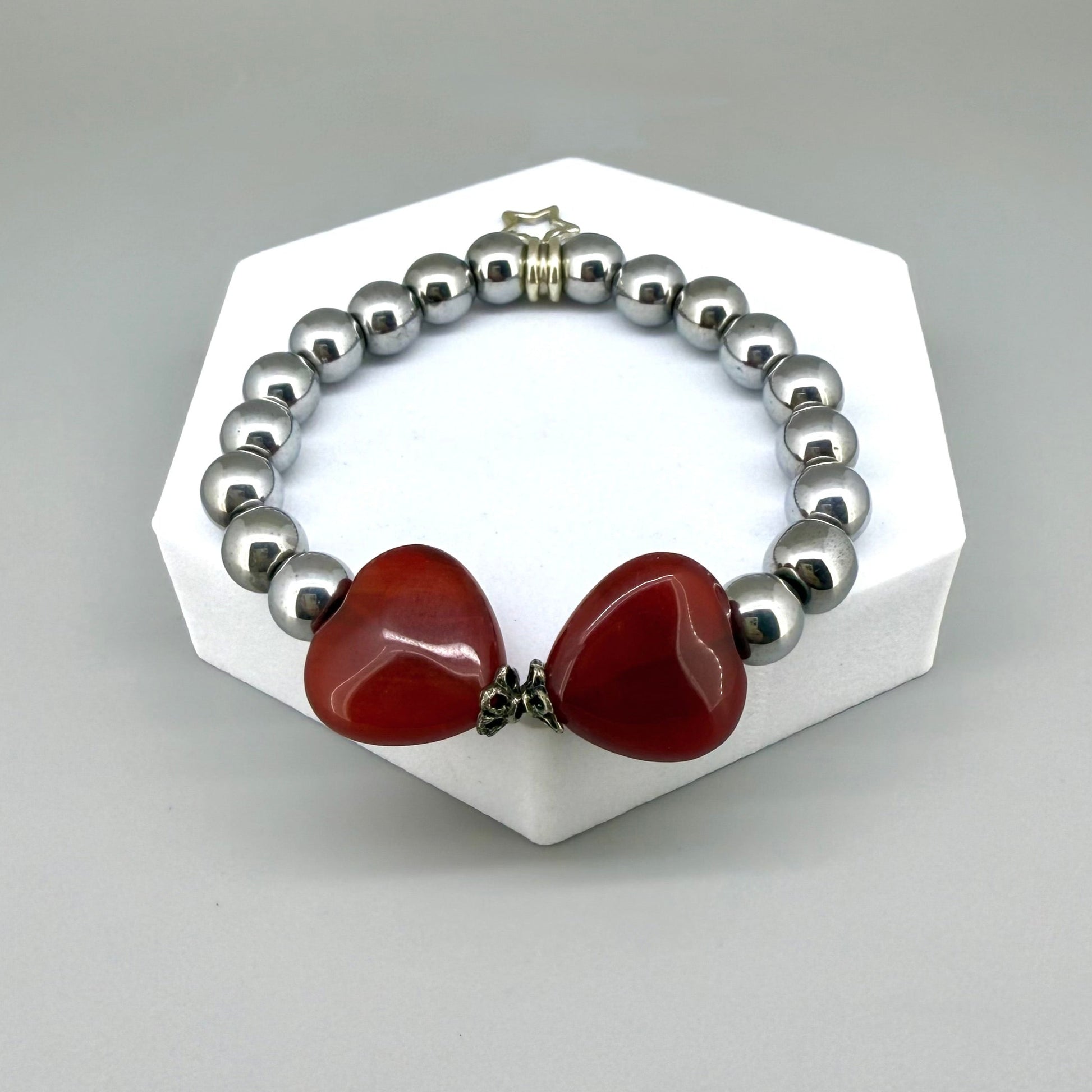 Silver hematite beaded bracelet, 18cm, metallic gemstone beads with two orange-red heart-shaped carnelian accents on elastic stretch band.