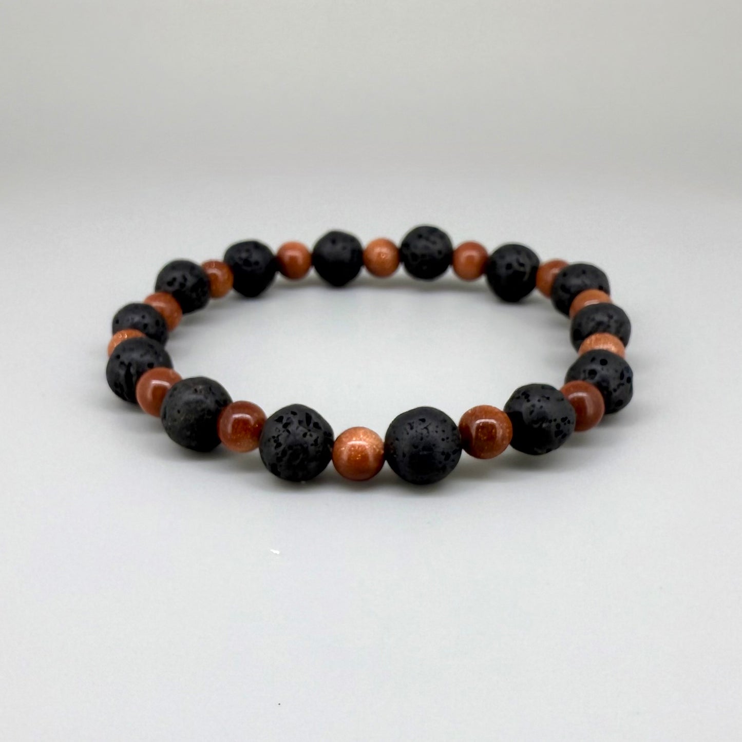 Lava and goldstone beaded bracelet, 18cm, alternating matte black lava beads and smaller shimmering golden-brown man-made goldstone beads on elastic stretch band.