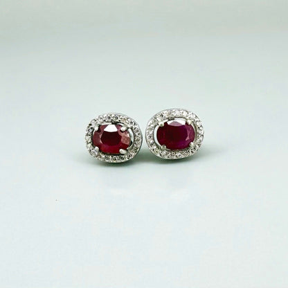 White gold plated sterling silver stud earrings with 2.6 ct natural rubies surrounded by cubic zirconia; classic halo design, elegant brilliance.