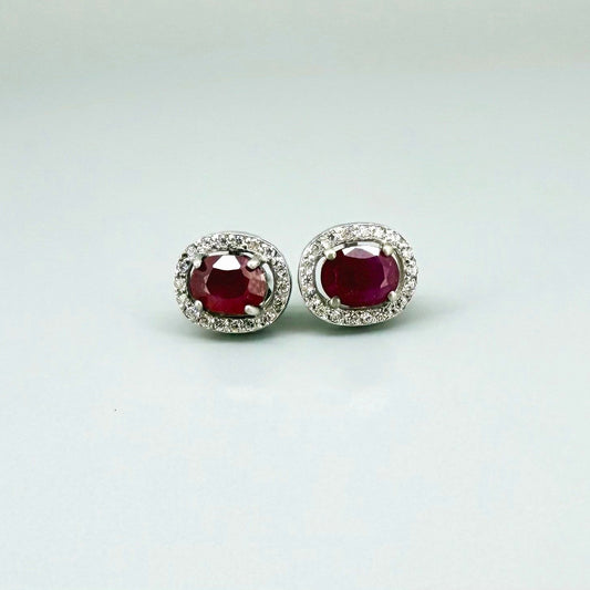 White gold plated sterling silver stud earrings with 2.6 ct natural rubies surrounded by cubic zirconia; classic halo design, elegant brilliance.