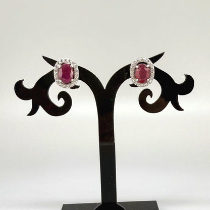 White gold plated sterling silver stud earrings with 2.6 ct natural rubies surrounded by cubic zirconia; classic halo design, elegant brilliance.