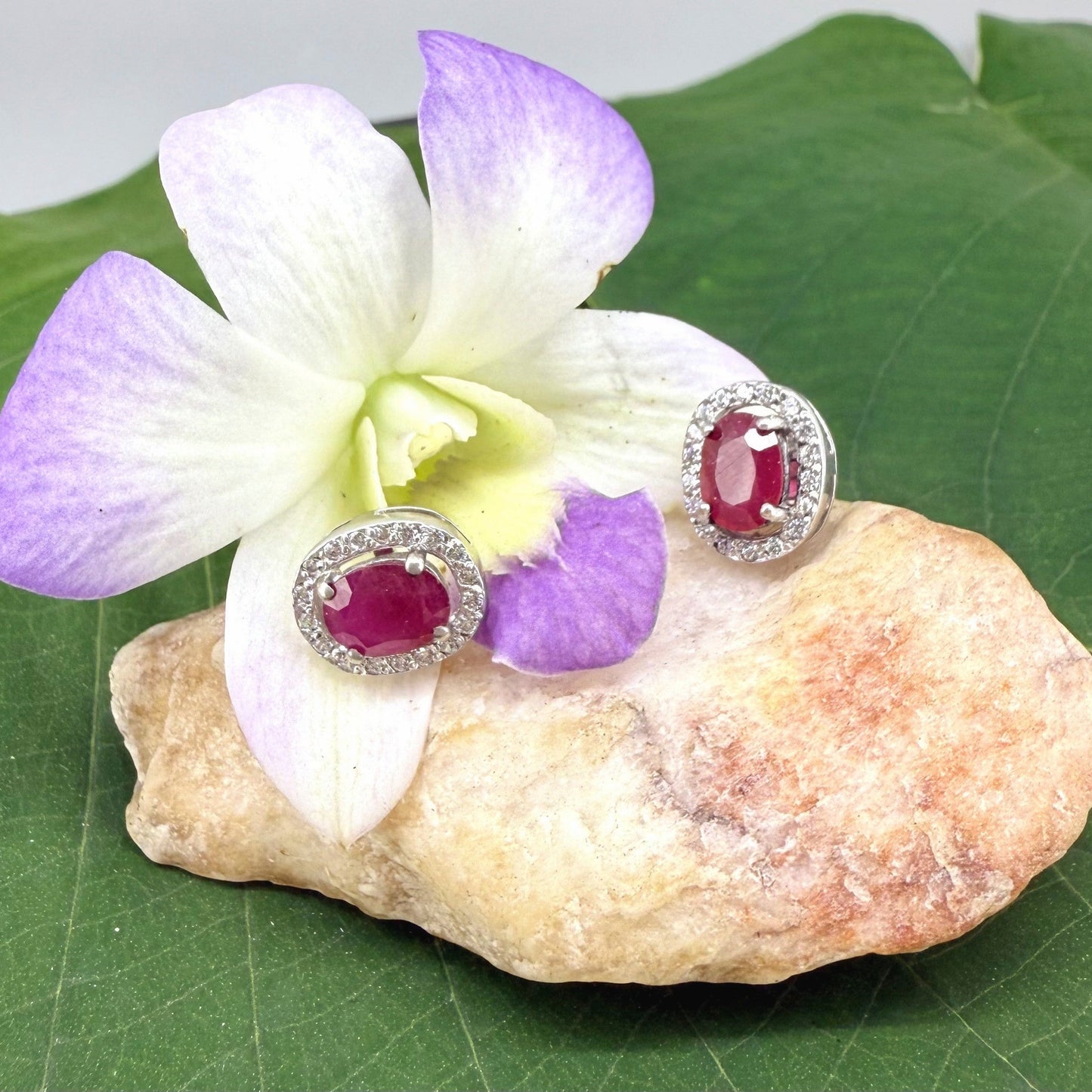White gold plated sterling silver stud earrings with 2.6 ct natural rubies surrounded by cubic zirconia; classic halo design, elegant brilliance.