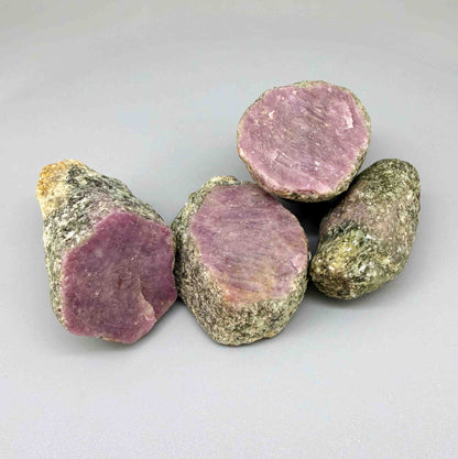 Natural ruby in grey-green host rock, uncut rough stones with pink to purplish-pink ruby sections.