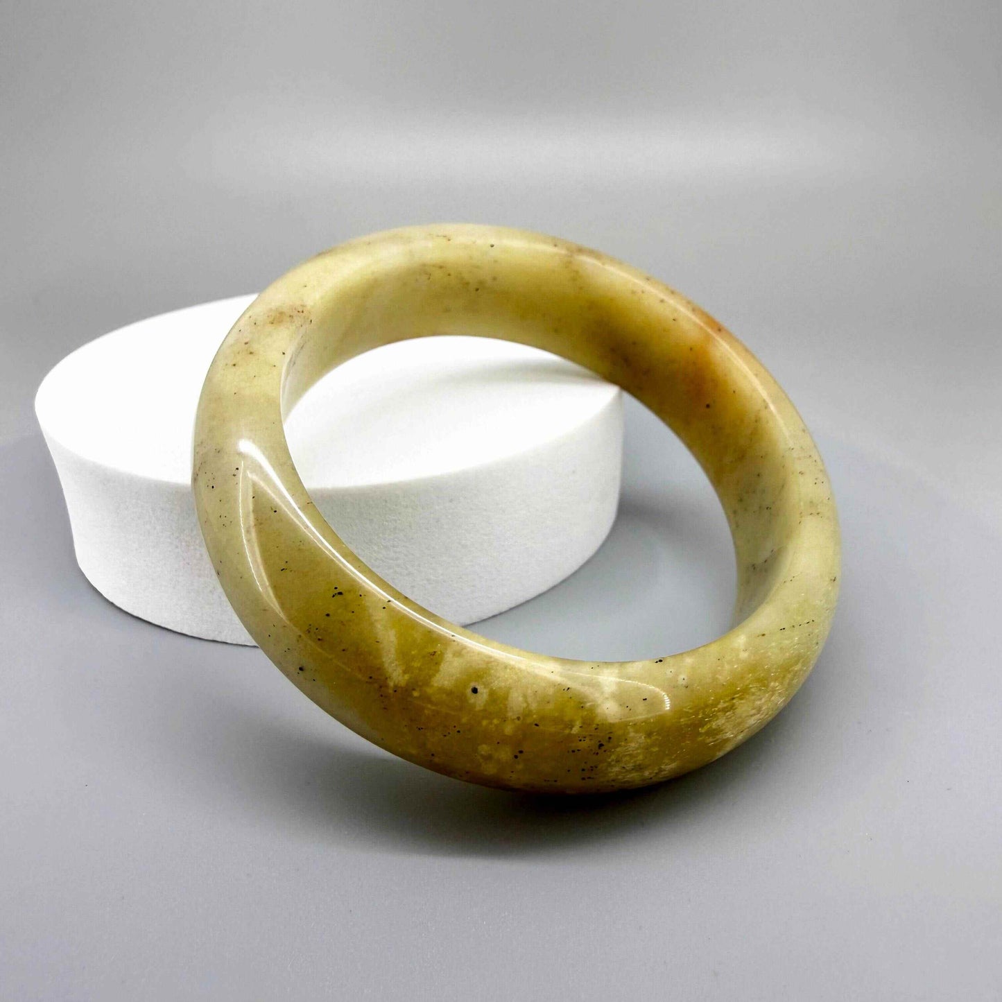 Polished jade bangle in soft earth tones with smooth surface and natural variations