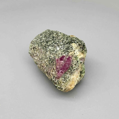 Natural ruby in matrix rough stone with grey-greenish host rock and vivid pink ruby core, uncut specimen.