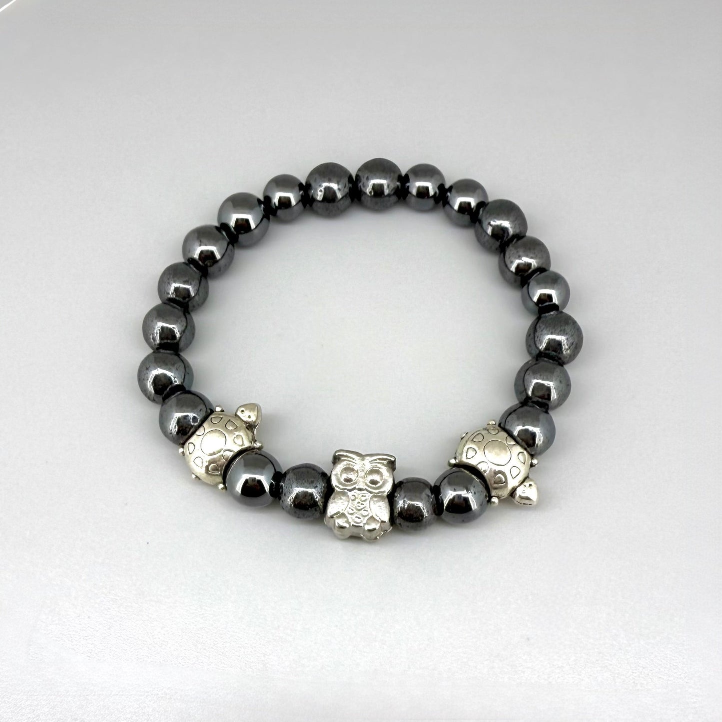 Hematite beaded bracelet, 18cm, metallic dark grey gemstone beads with two turtle accents and one owl charm on elastic stretch band.